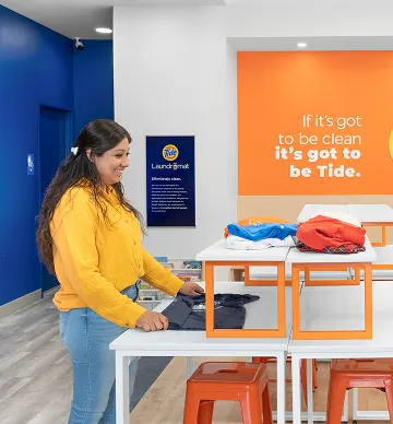 Store manager and customer smiling while folding clean laundry inside a laundromat.