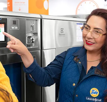 Empleado de Lavandería Tide ayudando a un cliente con la lavadora.