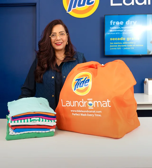 Empleado de Lavandería Tide con ropa limpia y doblada en el mostrador.