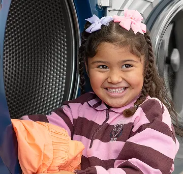 Niña sacando ropa limpia de una secadora de Lavandería Tide.