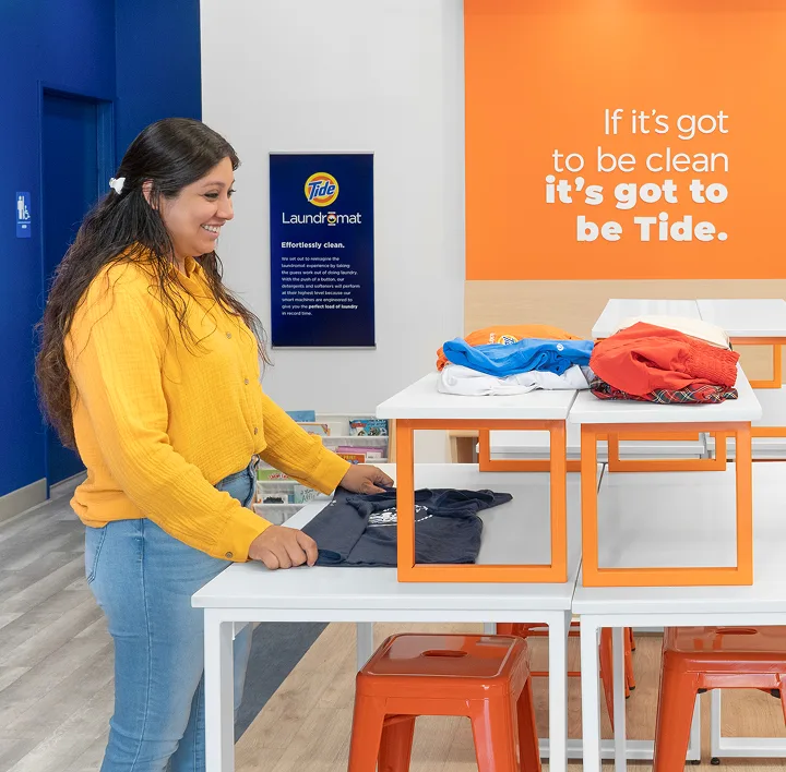Store manager and customer smiling while folding clean laundry inside a laundromat.