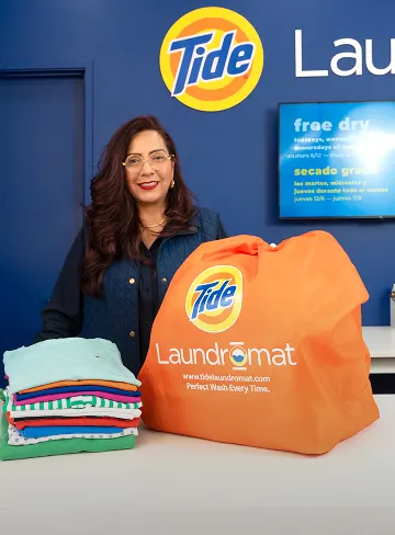 Empleado de Lavandería Tide con ropa limpia y doblada en el mostrador.