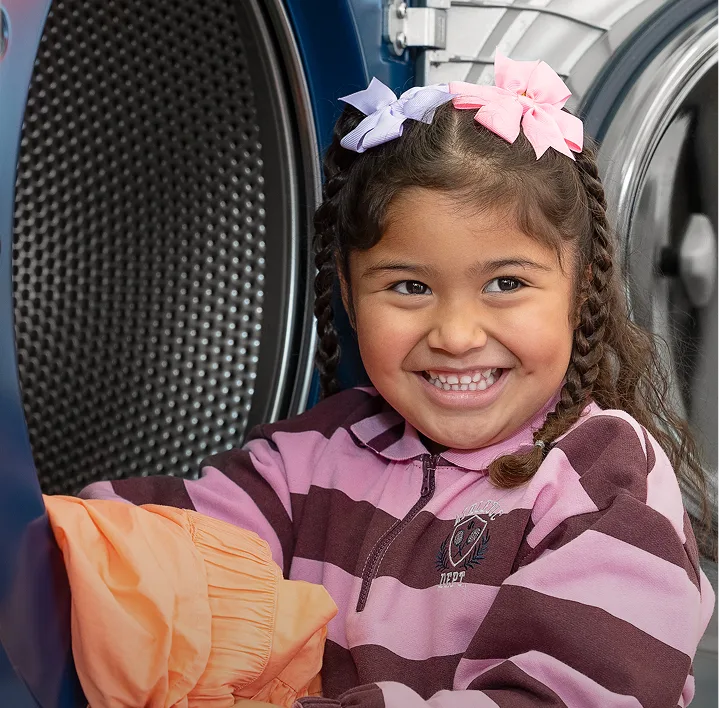 Niña sacando ropa limpia de una secadora de Lavandería Tide.