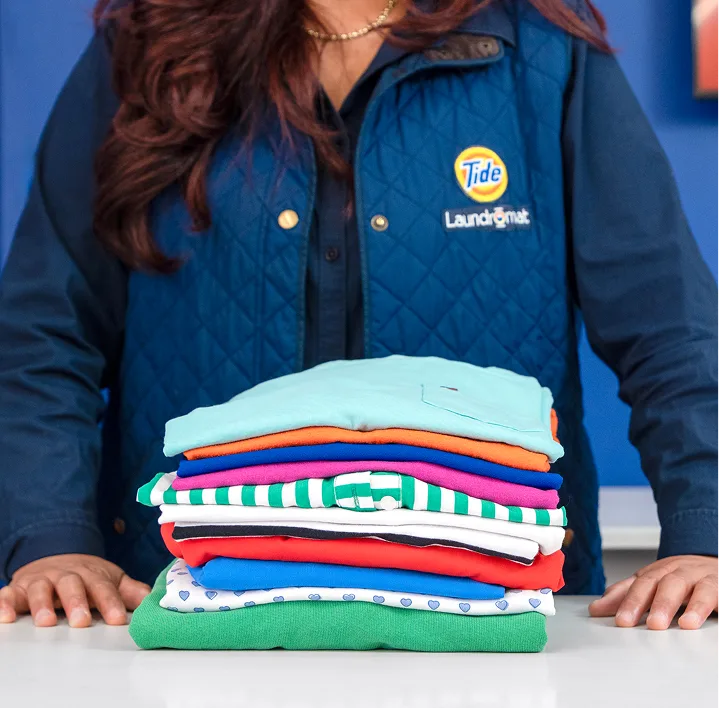 Empleado de Lavandería Tide mostrando ropa doblada.