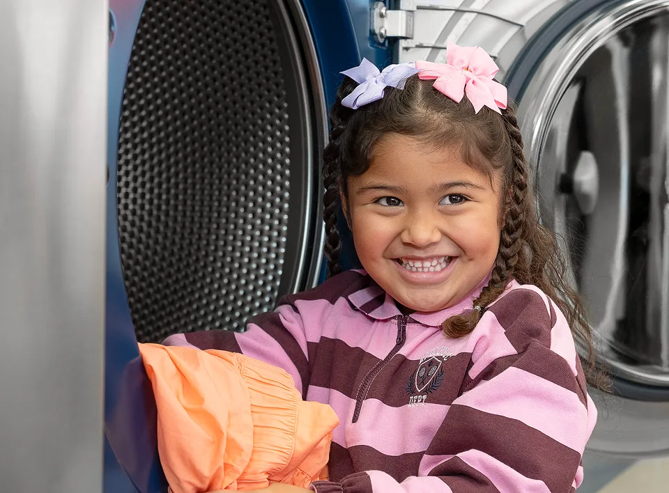 Niña sacando ropa limpia de una secadora de Lavandería Tide.
