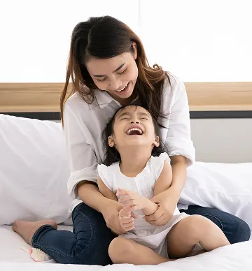 Madre e hija sonriendo sobre sábanas blancas limpias.