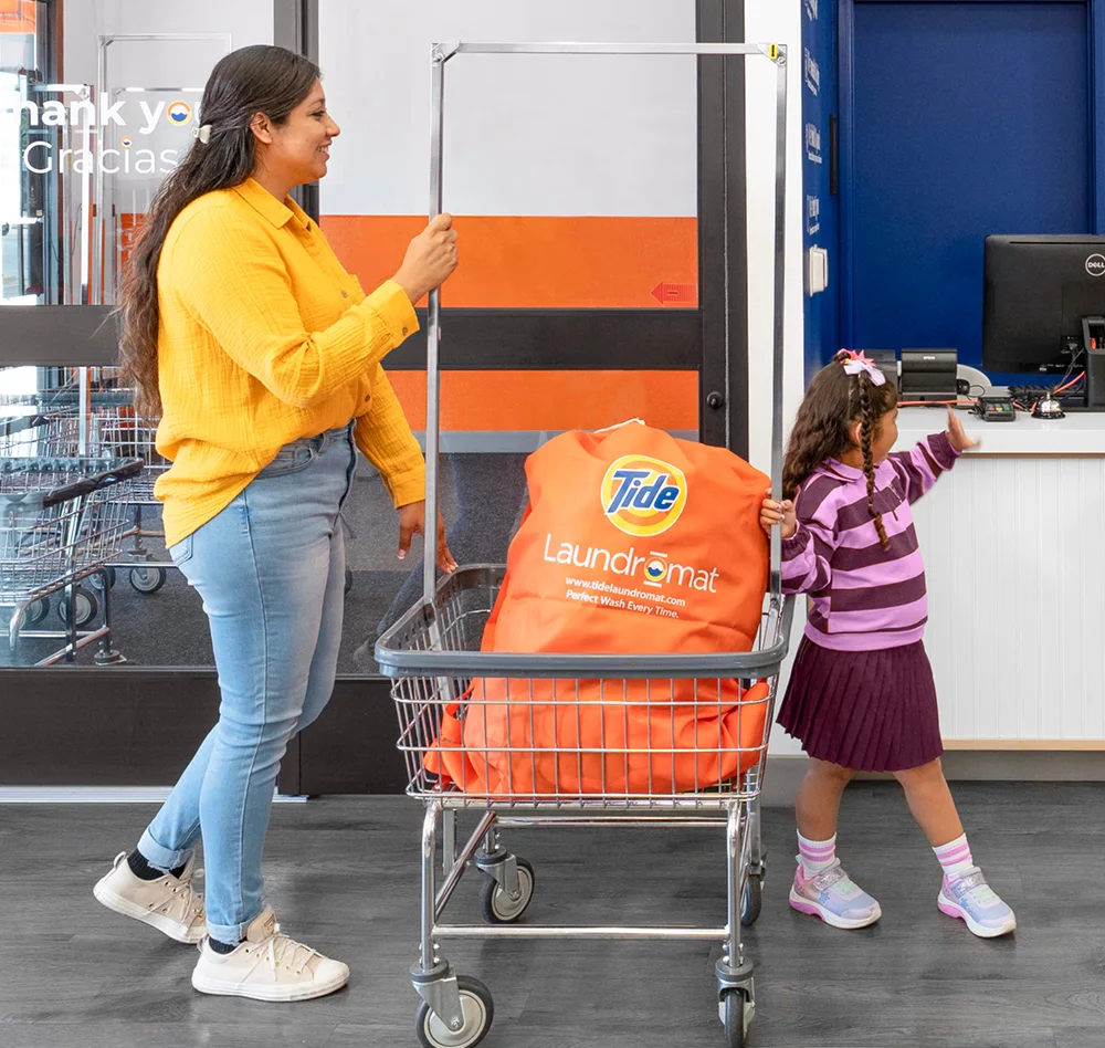 Parent and child walking into tide laundromat with laundry to wash