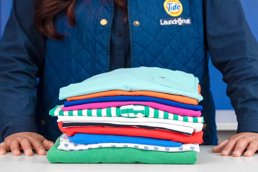 Empleado de Lavandería Tide mostrando ropa doblada.