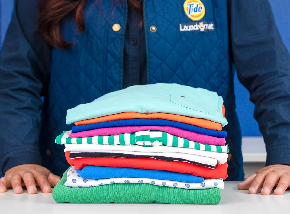 Empleado de Lavandería Tide mostrando ropa doblada.