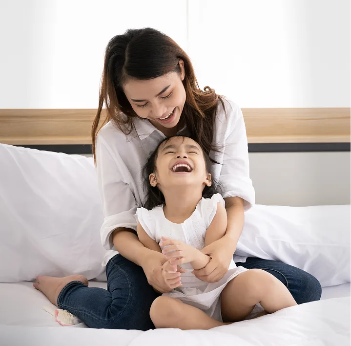 Madre e hija sonriendo sobre sábanas blancas limpias.