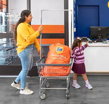Parent and child walking into tide laundromat with laundry to wash