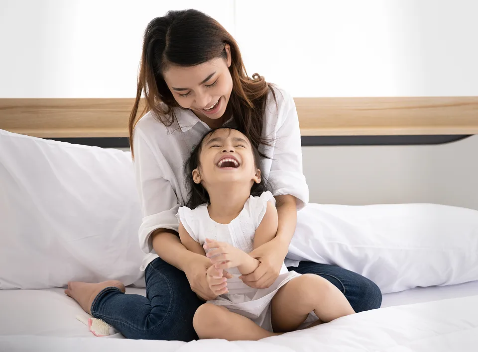 Madre e hija sonriendo sobre sábanas blancas limpias.