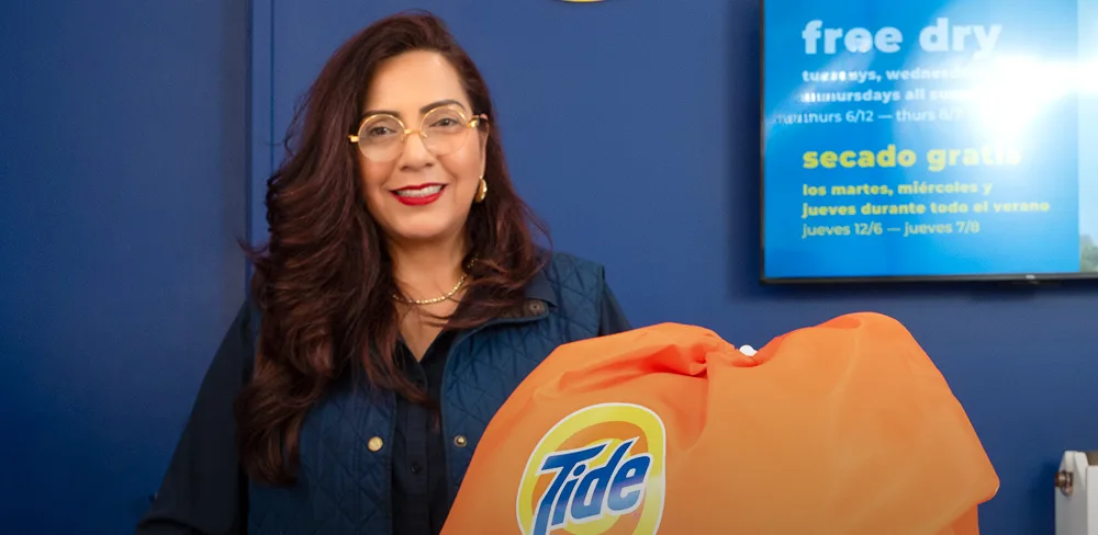 Empleado de Lavandería Tide con ropa limpia y doblada en el mostrador.