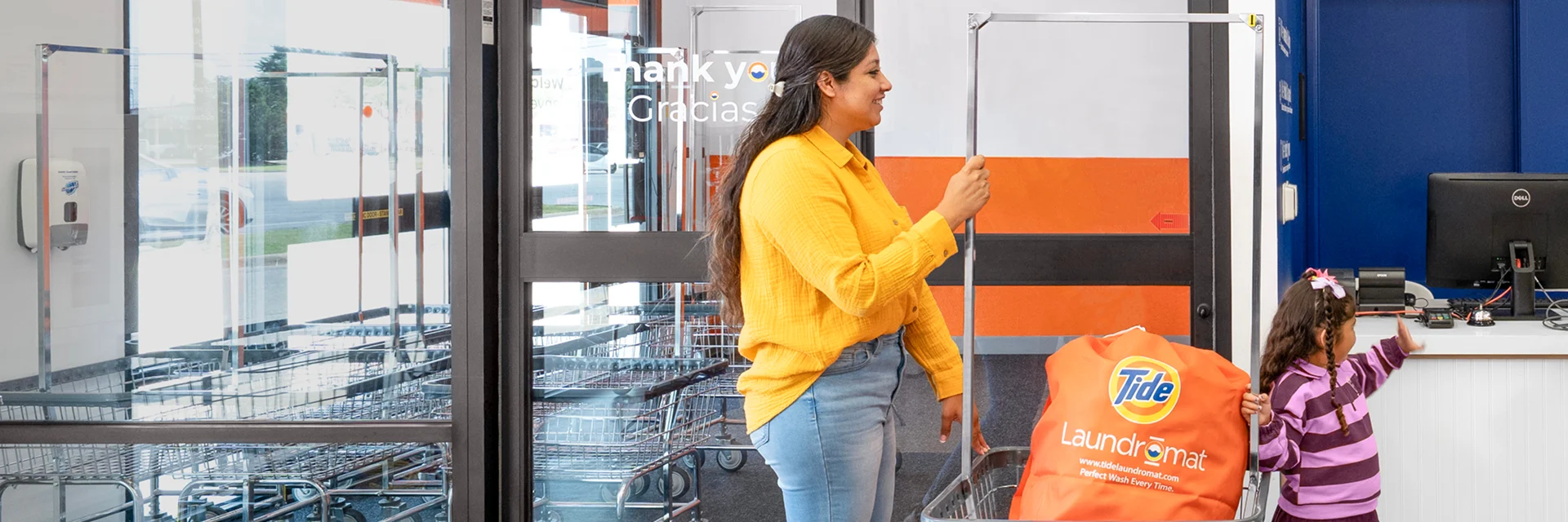 Parent and child walking into tide laundromat with laundry to wash