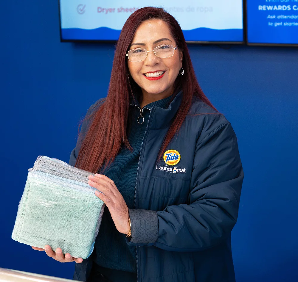 Empleado de Lavandería Tide mostrando toallas recién dobladas.