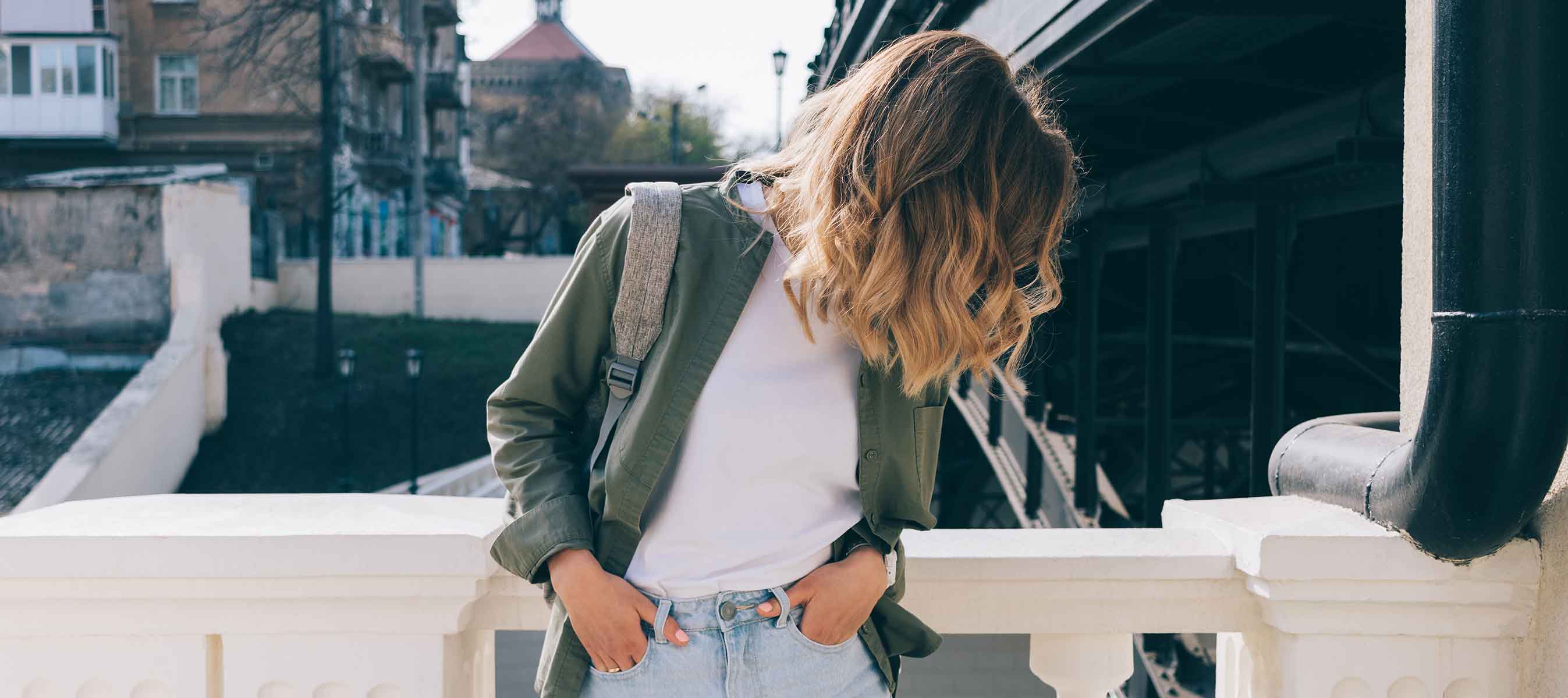 Dirty blonde girl with dry hair in green jacket with hands in pockets of her jeans next to a bridge Dirty blonde girl with dry hair in green jacket with hands in pockets of her jeans next to a bridge