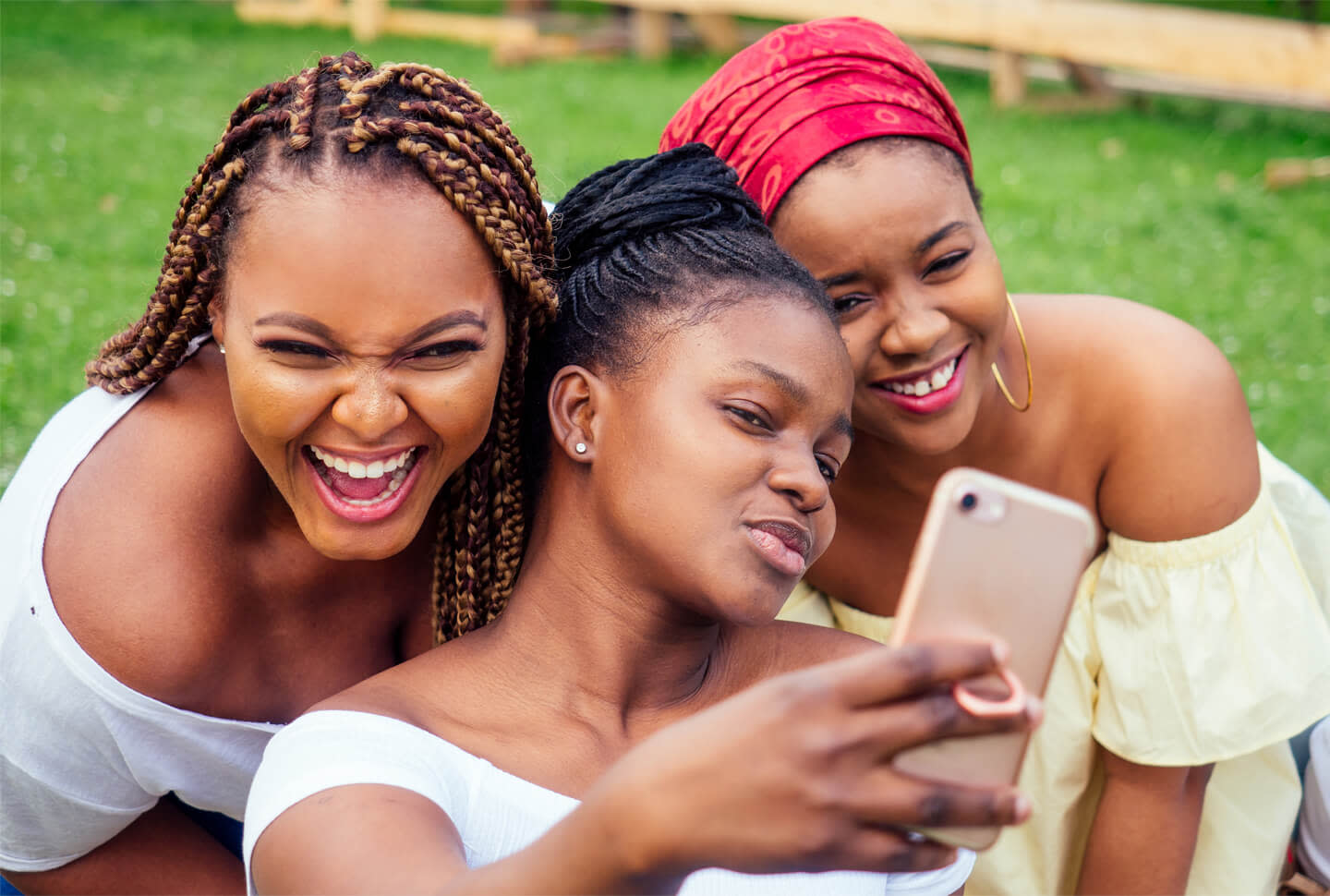 Picture of three beautiful African-American women with box braids, locs, and a turban, taking selfies on a cell phone in the park Picture of three beautiful African-American women with box braids, locs, and a turban, taking selfies on a cell phone in the park