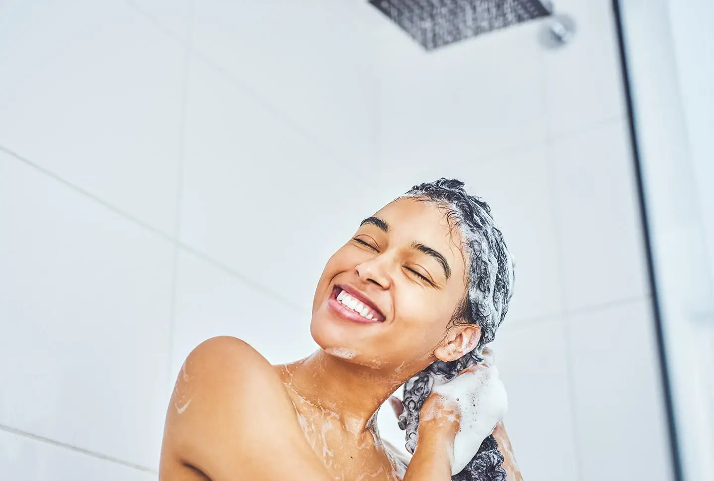 A woman with curly hair smiling in the shower, using H&S shampoo to achieve healthy hair. A woman with curly hair smiling in the shower, using H&S shampoo to achieve healthy hair.