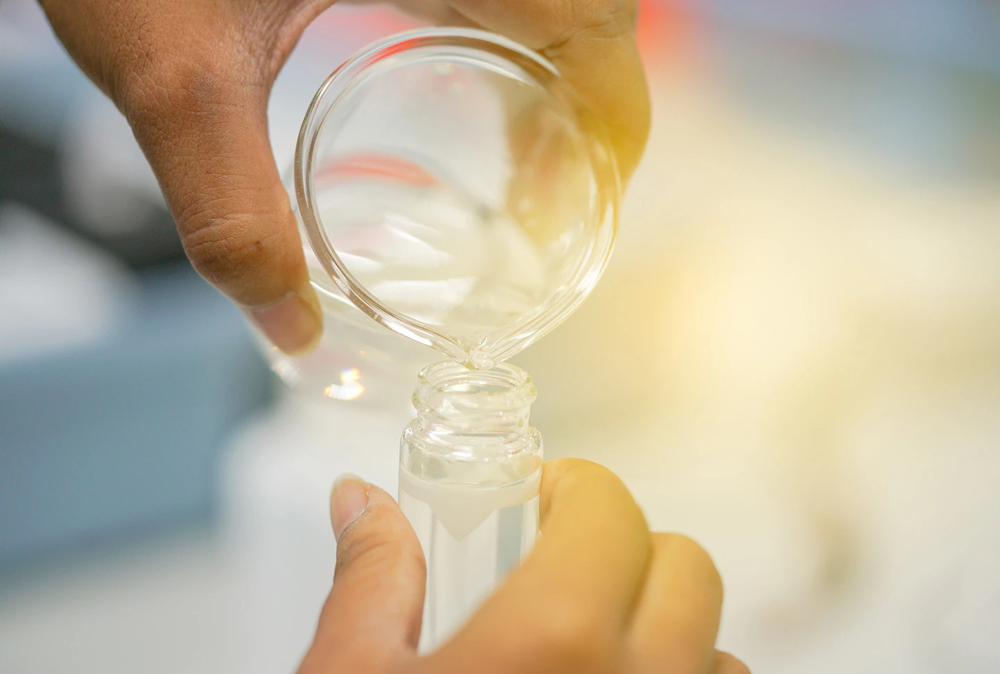 A tan-skinned hand holding a glass beaker pours clear liquid into a glass tube in a lab, illustrating the formulation of anti-dandruff ingredients for effective scalp treatment. A tan-skinned hand holding a glass beaker pours clear liquid into a glass tube in a lab, illustrating the formulation of anti-dandruff ingredients for effective scalp treatment.