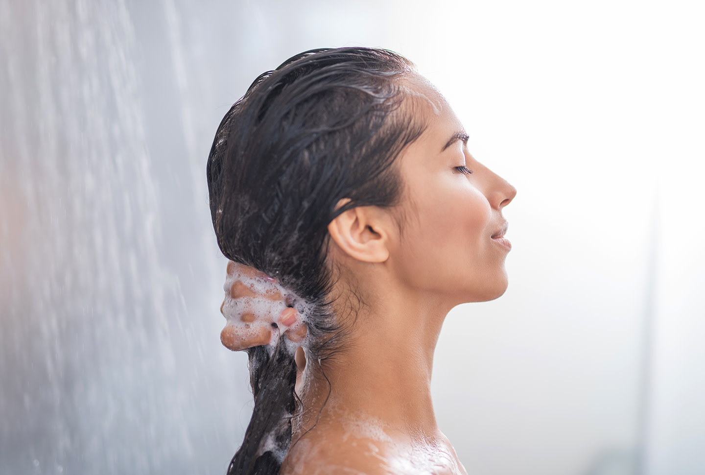 Side view of calm brunette girl using sulfate free dandruff shampoo during a shower. Side view of calm brunette girl using sulfate free dandruff shampoo during a shower.