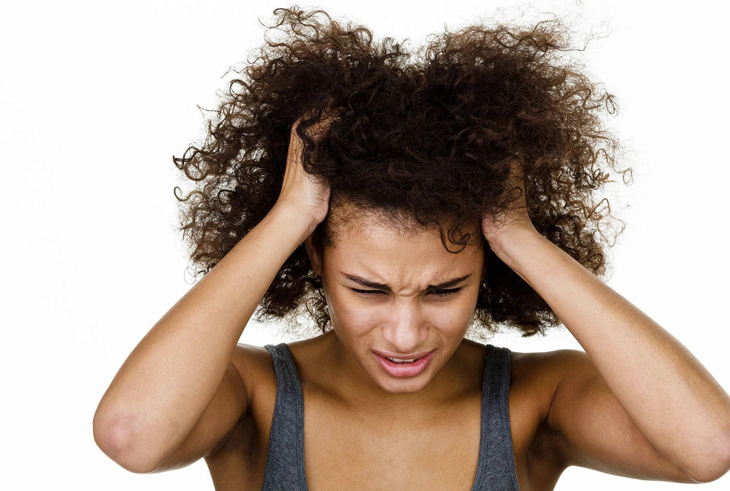 A tan-skinned woman with distressed look has hands in her brown hair itching her scalp in front of a white background. A tan-skinned woman with distressed look has hands in her brown hair itching her scalp in front of a white background.