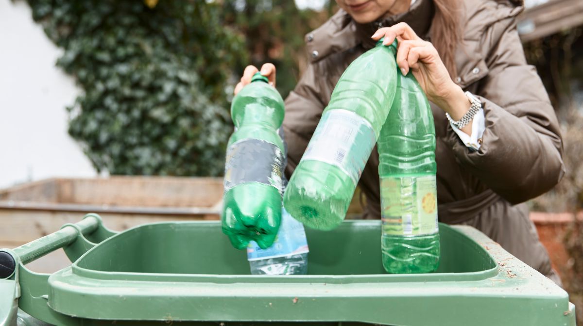 Green colored plastic bottles being put in a recycling bin