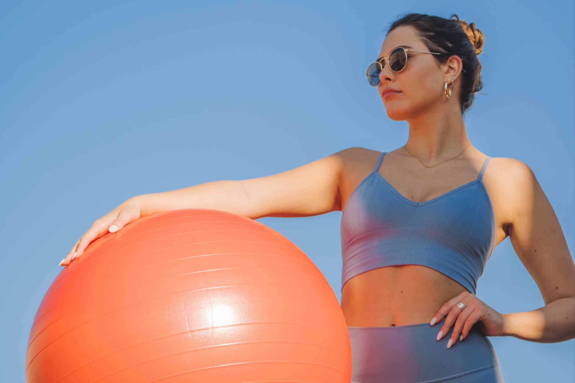 Woman wearing athletic clothes holds exercise ball. 