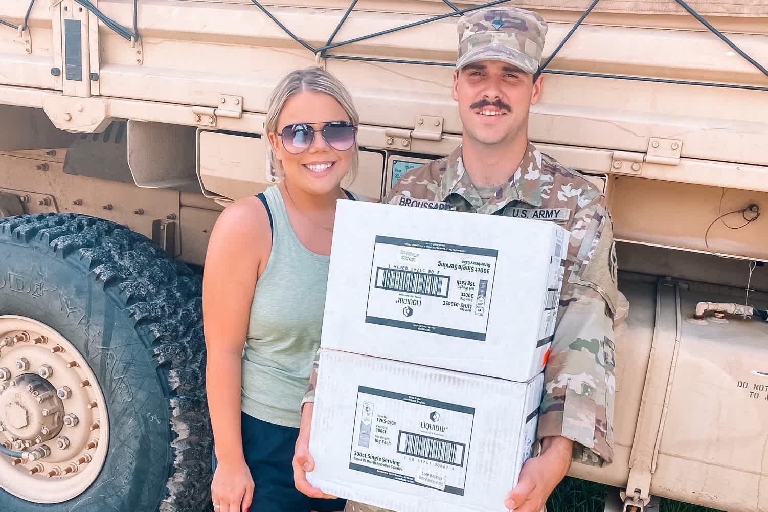 Young woman and man wearing army fatigues holding a case of Liquid I.V. Hydration Multiplier. 