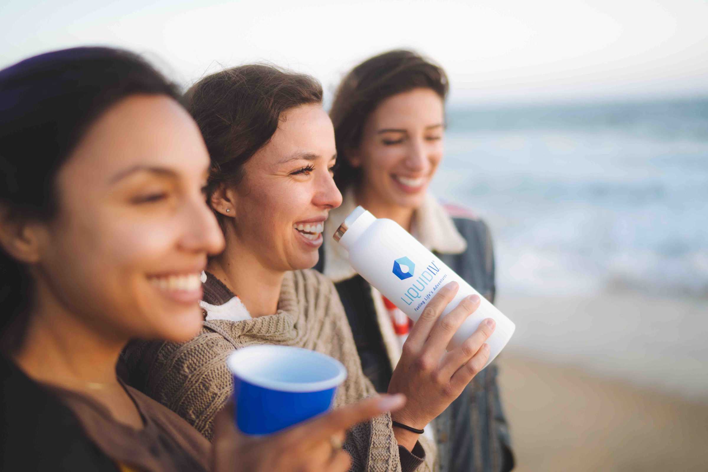 Three sisters drink Liquid I.V. on the beach in wintertime. 