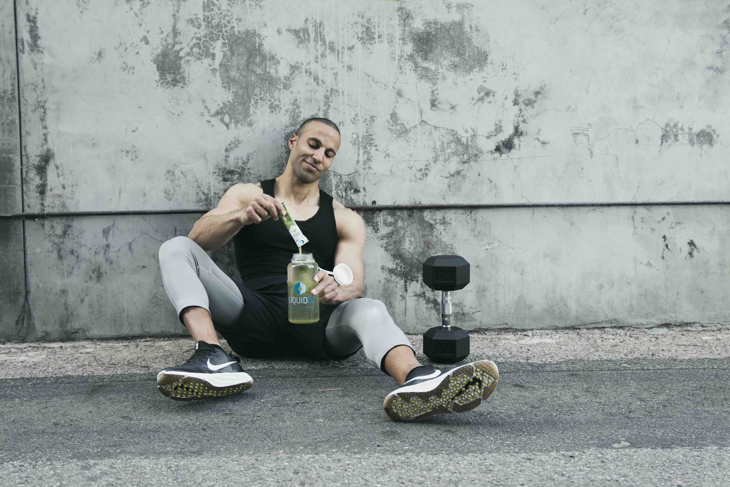 Man wearing athletic gear pours a stick of Energy Multiplier into a bottle of water. 