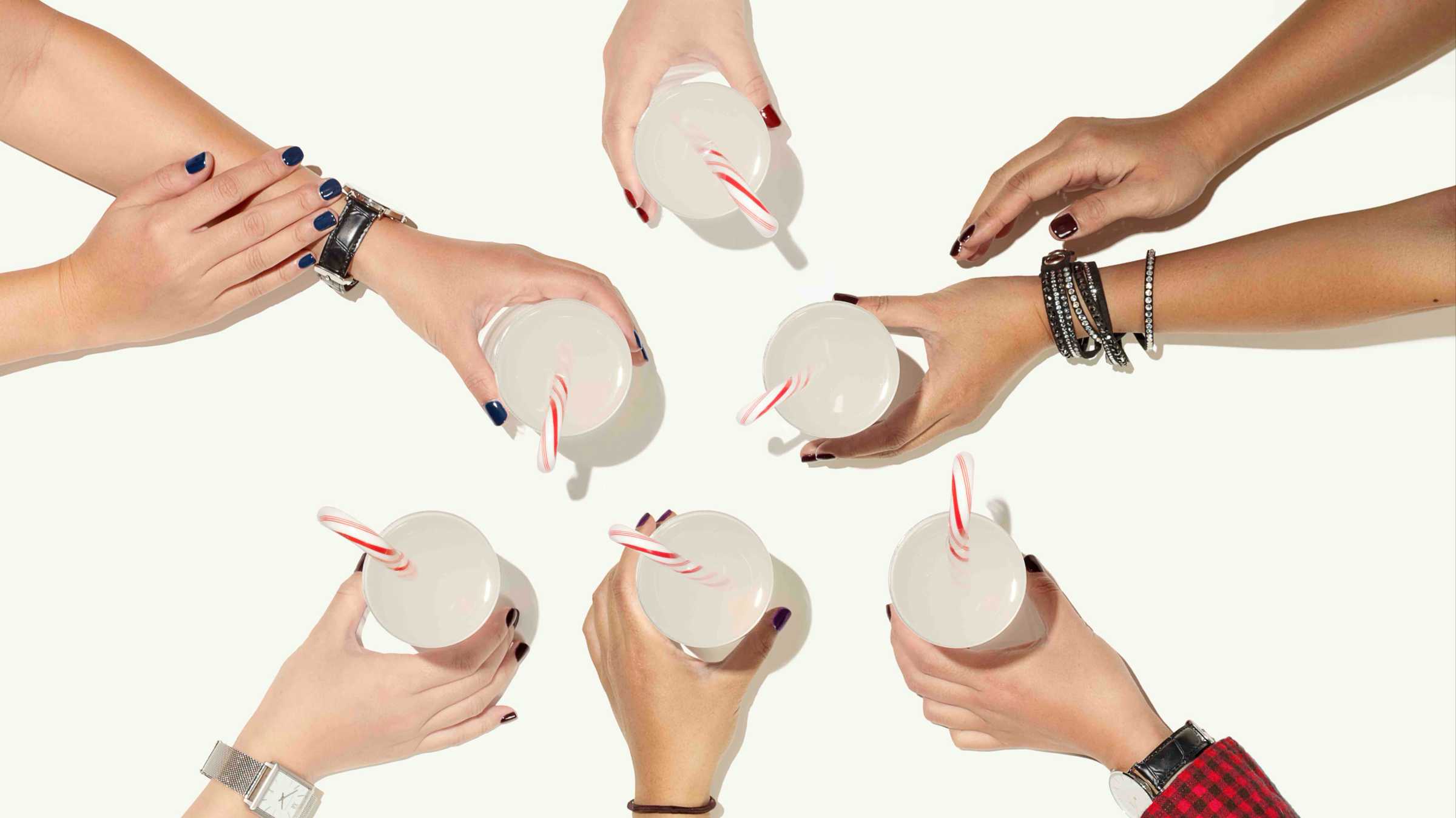 White backdrop with six hands holding drinks arranged in the shape of a Christmas tree. 