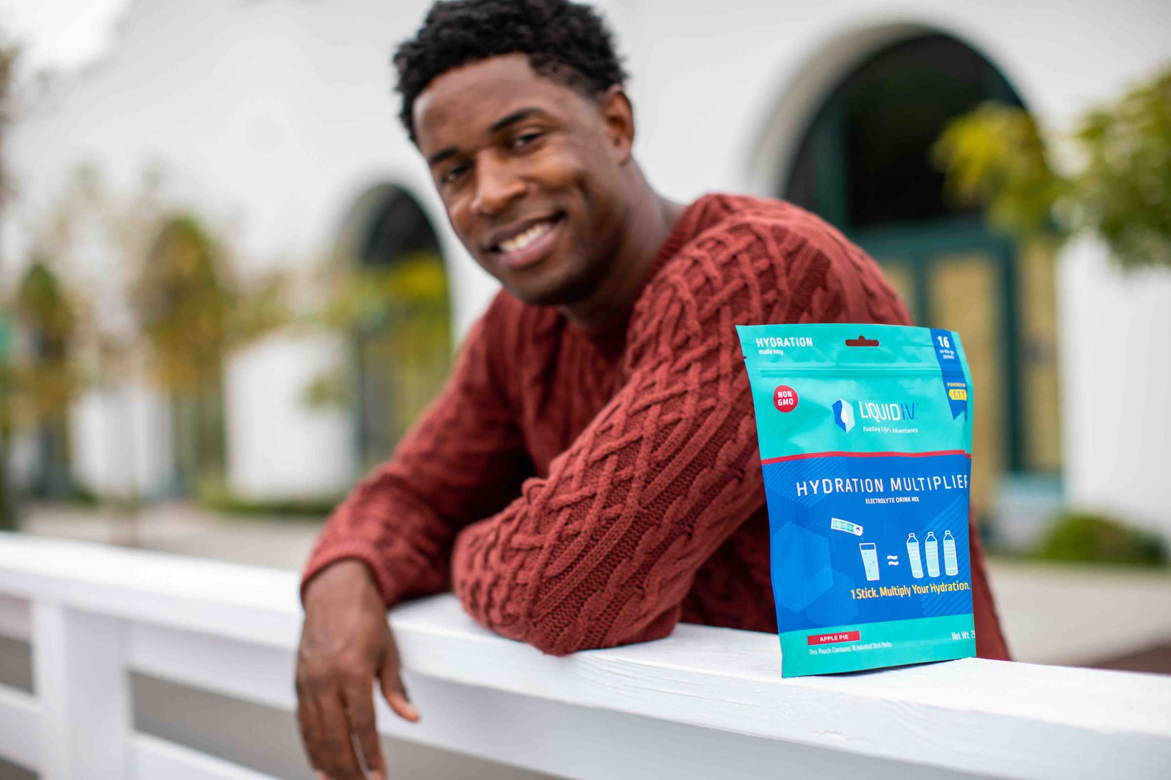 Young man wearing a red sweater smiles while posing with Liquid I.V. Hydration Multiplier.