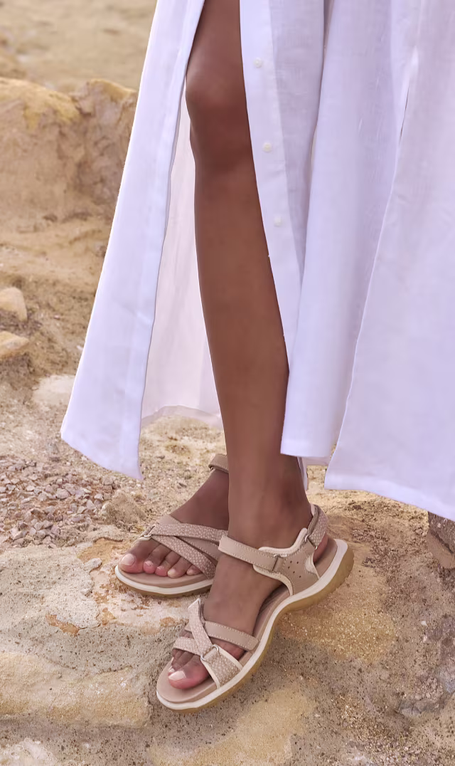 Beige Offroad Roam-sandaler i skinn til dame fra ECCO på steinete underlag, stylet med en lang hvit kjole.