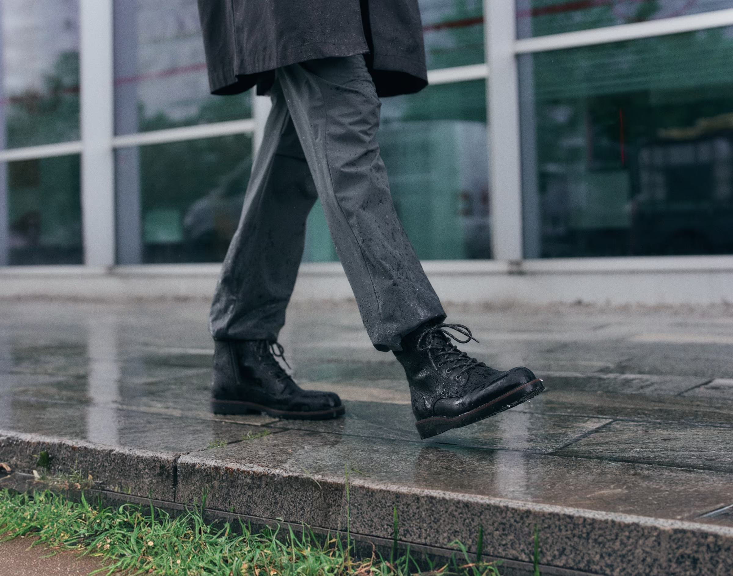 Person i sorte snørestøvler i læder og grå bukser på et vådt fortov i regnvejr	Persoon met zwarte leren veterschoenen en een grijze broek die in de regen over een nat trottoir loopt