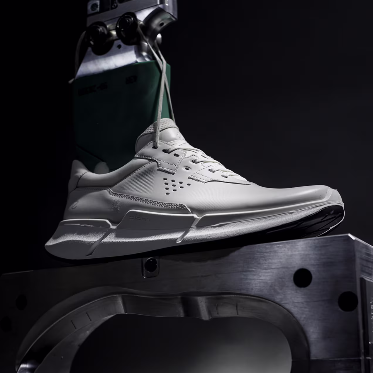 Side view of a white ECCO shoe positioned on a metal mold, illustrating the direct injection process of FLUIDFORM technology against a dark background.
