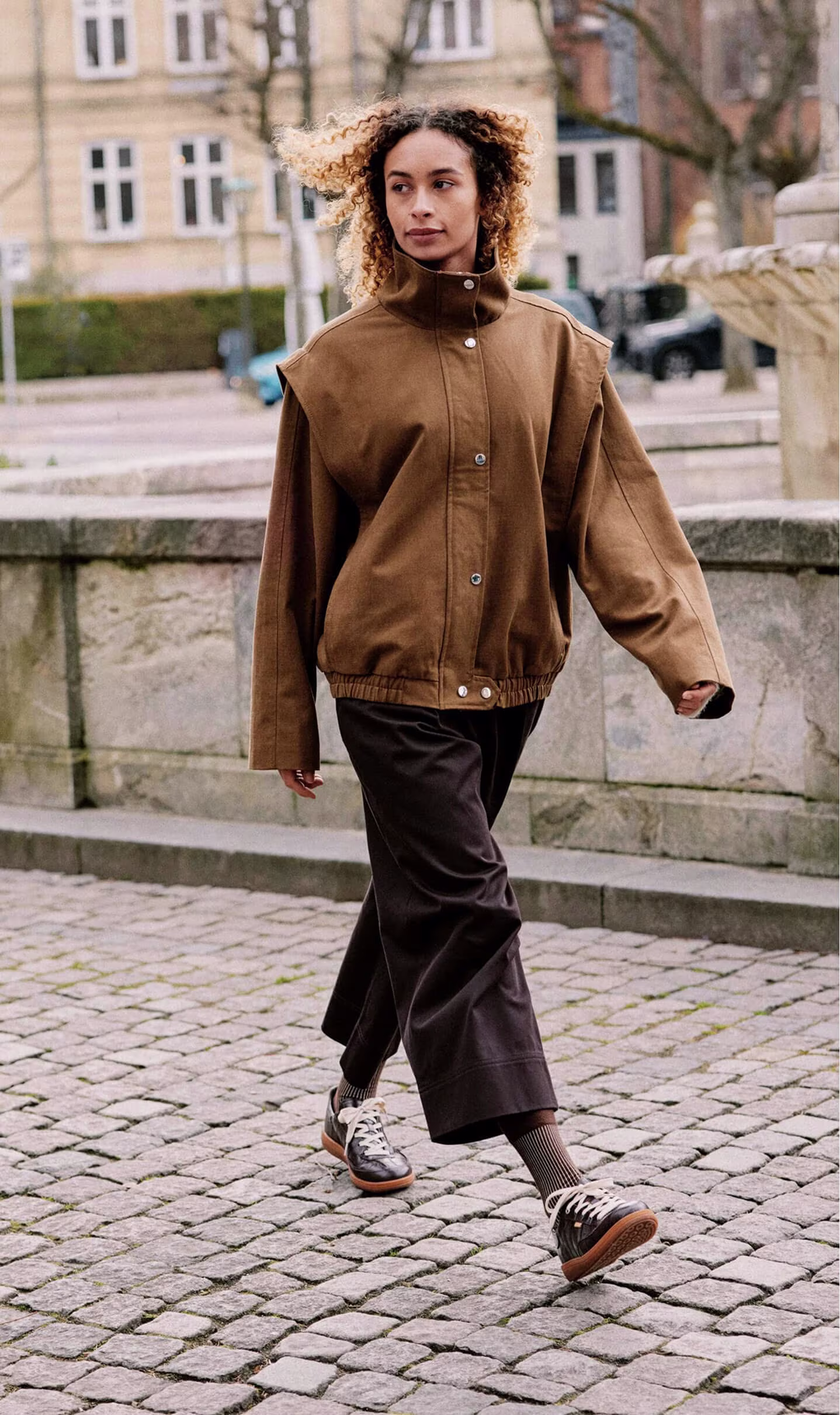 Woman walking in ECCO dark brown leather lace-up casual sneakers with gum soles on cobblestone street