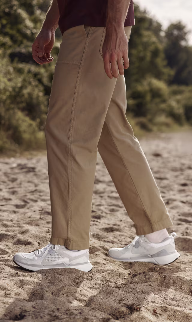 ECCO BIOM men's white athletic sneakers in premium mesh and leather walking on a sandy beach path.