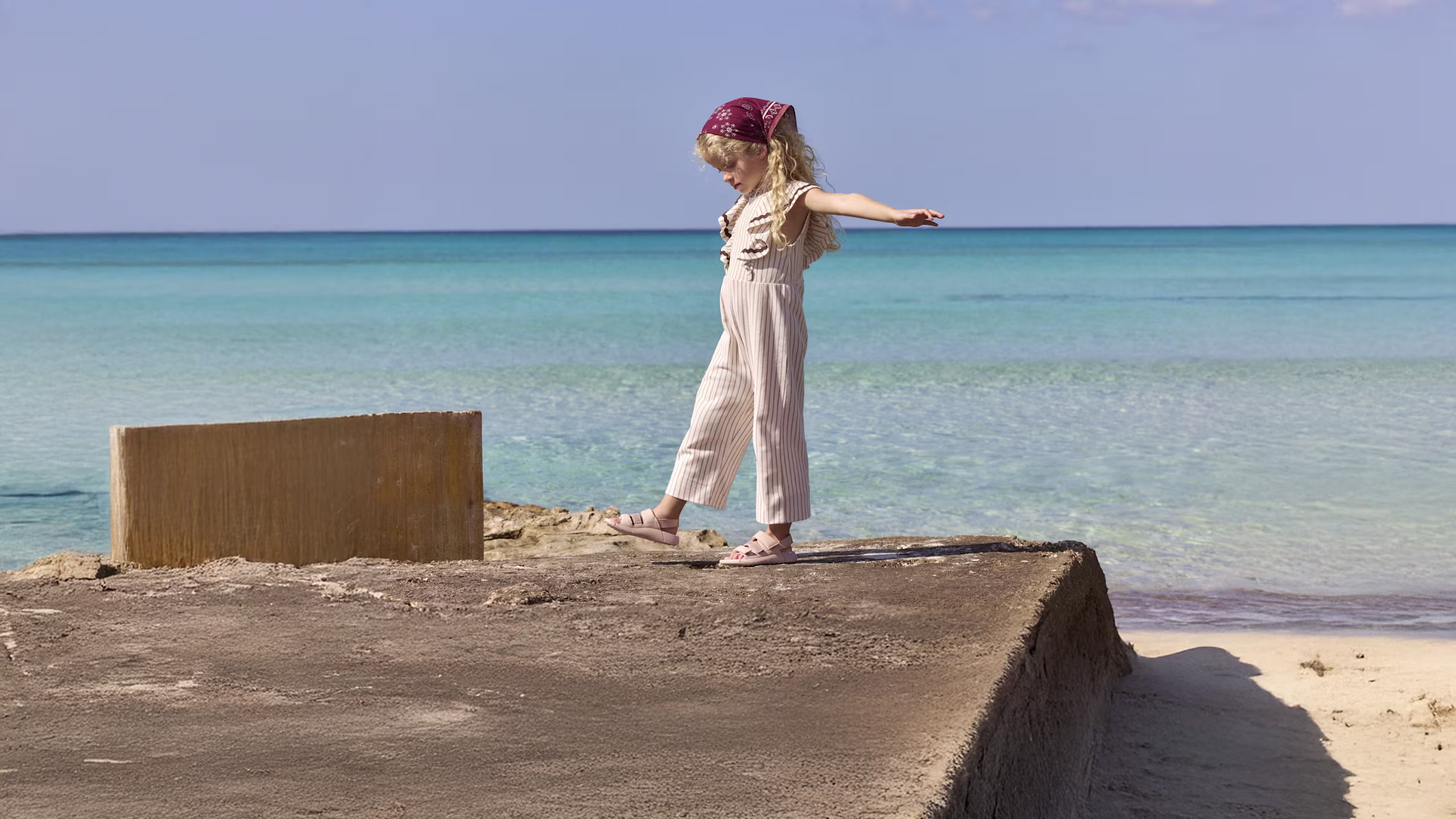 Girl balancing on a concrete block wearing ECCO double-strap leather sandals by the ocean.