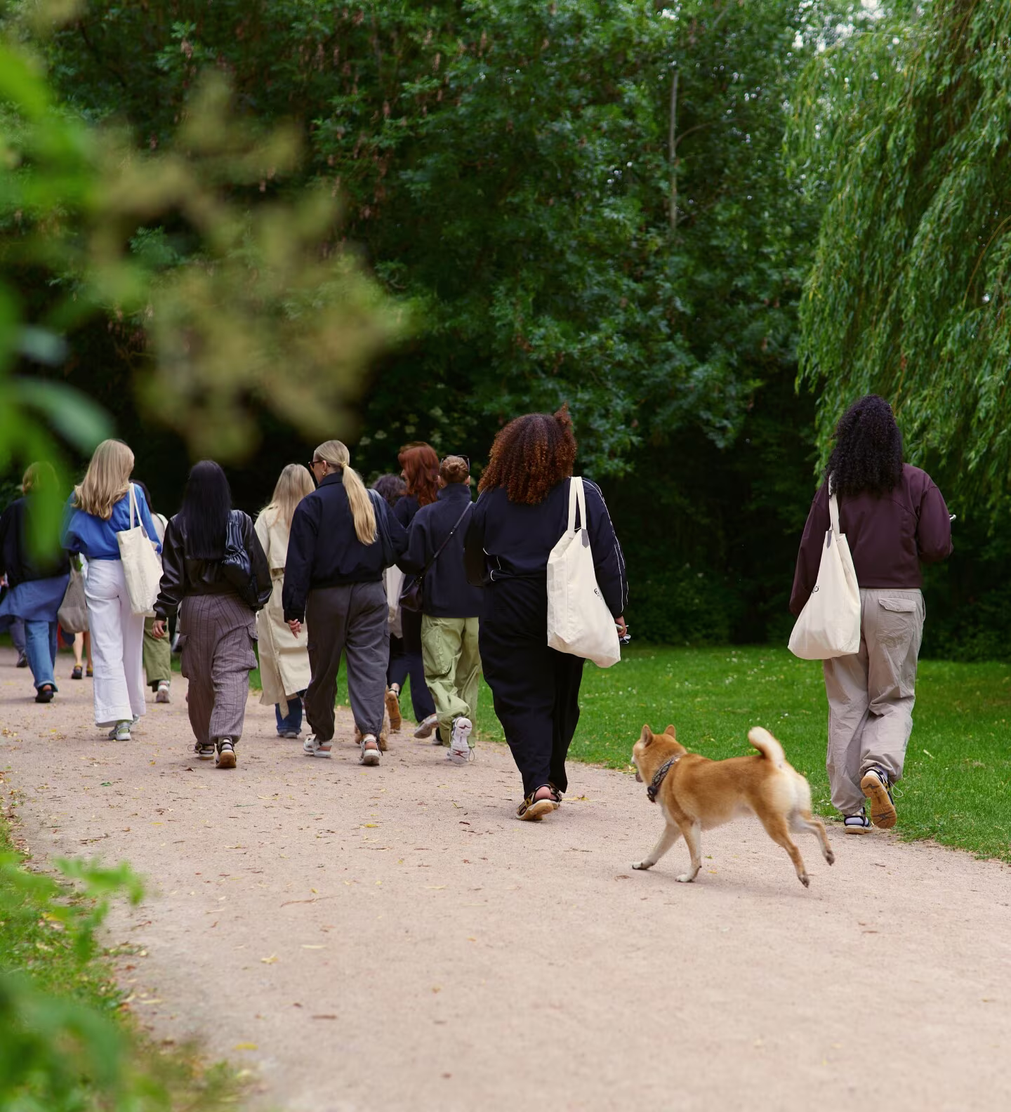 Eine stilvolle Gruppe genießt einen gemeinsamen Spaziergang in bequemen ECCO-Freizeitschuhen und mit ECCO-Canvas-Taschen. Müheloser skandinavischer Stil trifft auf den Alltag im Park.