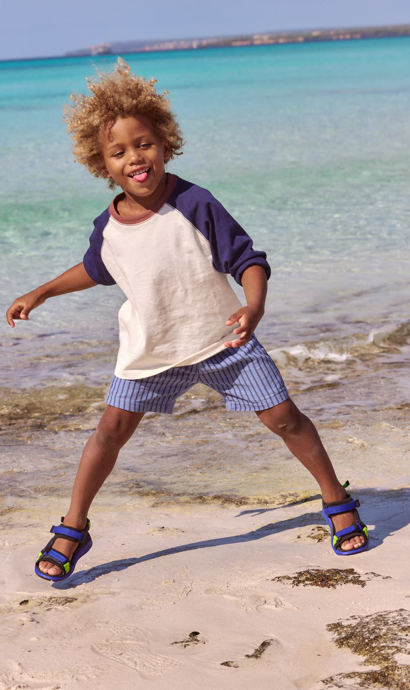 Blaue ECCO Sandalen für Kinder mit grünen Akzenten und verstellbaren Riemen, getragen von einem Kind am Sandstrand.