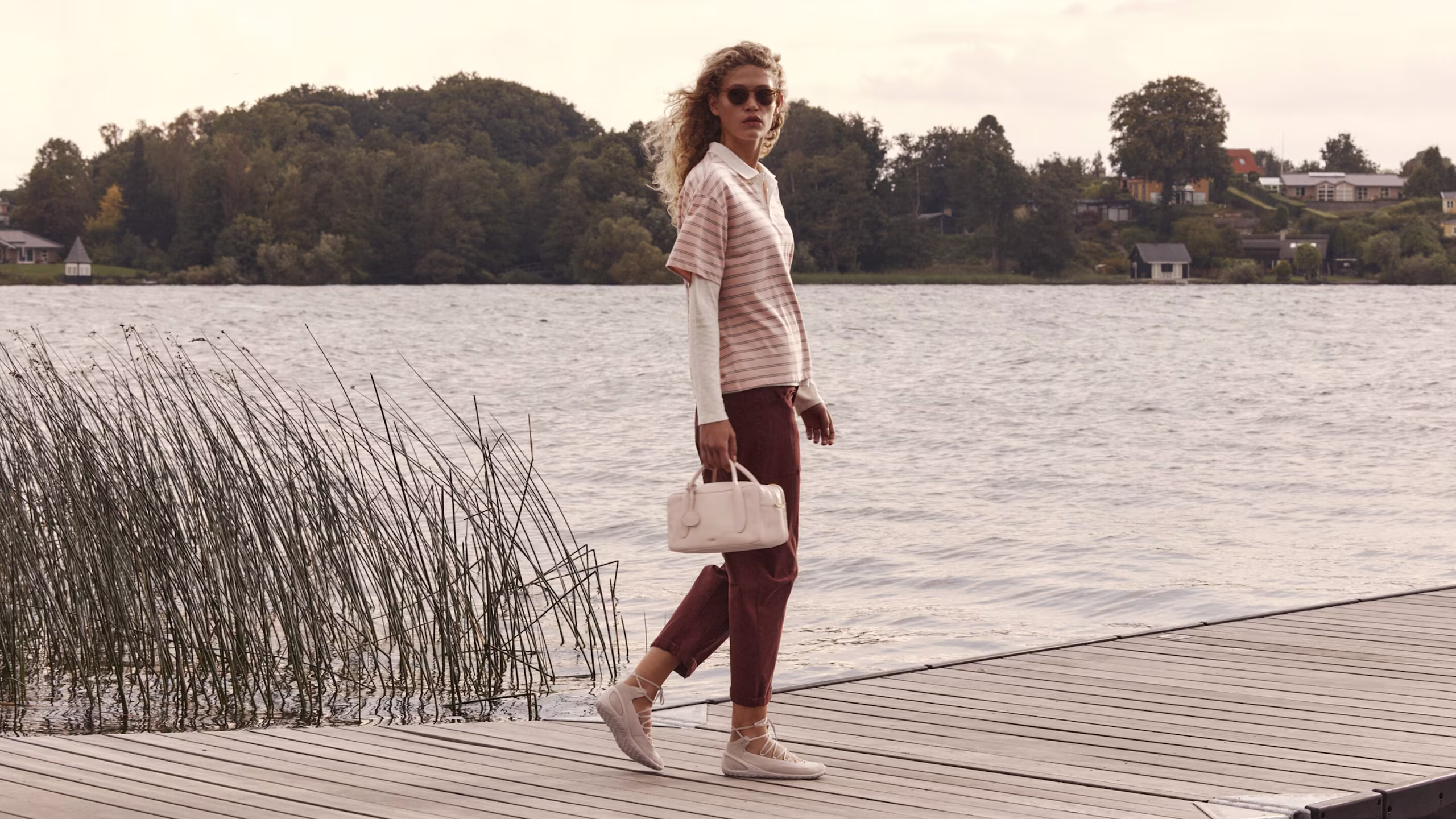 Woman on a wooden pier wearing light pink lace-up ballet flats and carrying a matching leather handbag.