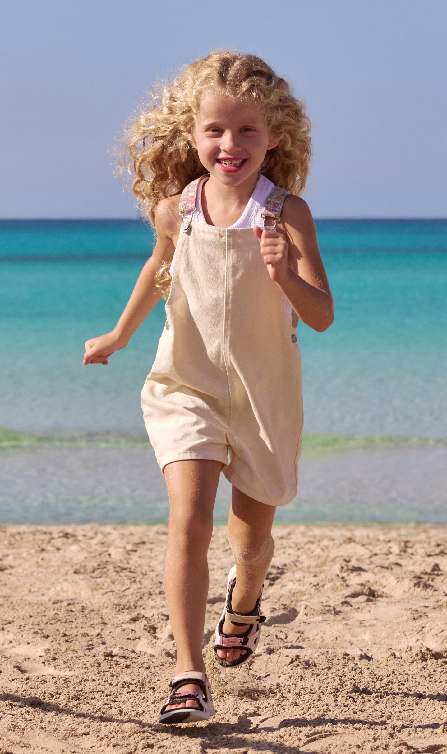 Pink-schwarze ECCO Funktionssandalen für Kinder mit verstellbaren Riemen, getragen von einem Kind beim Laufen am Strand.