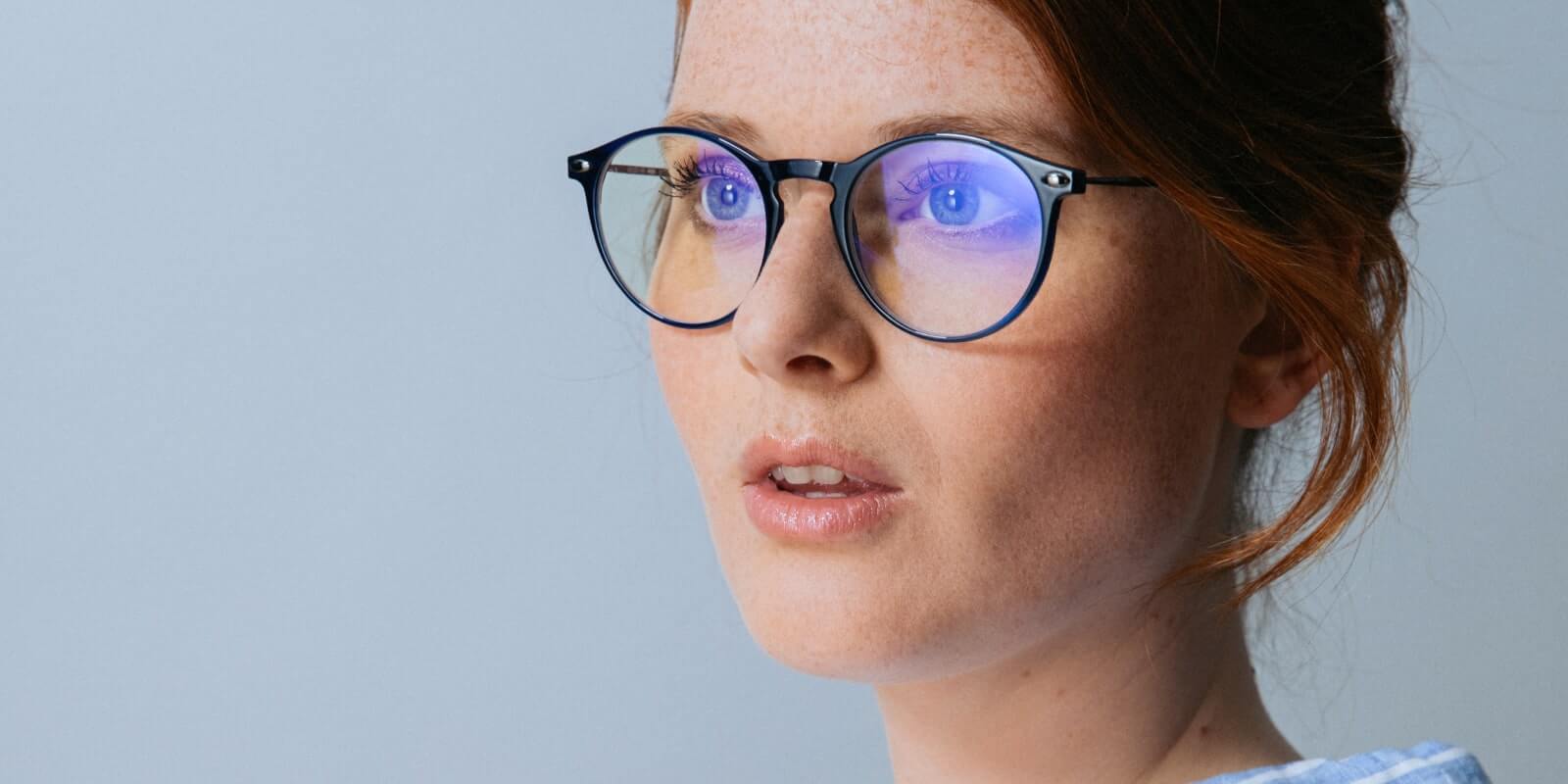 Blue anti-light glasses of round shape worn by a red-haired woman