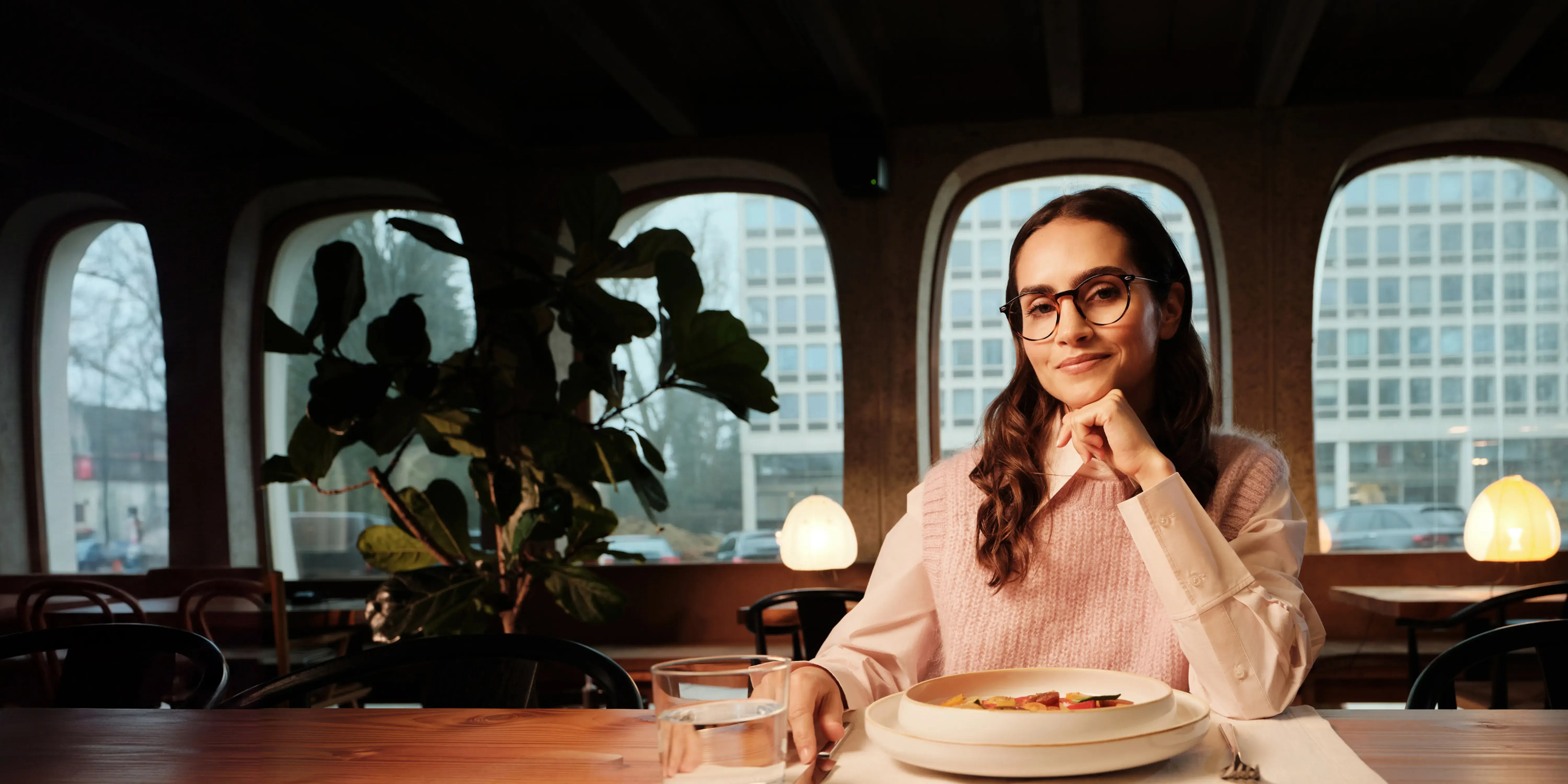 Woman wearing Multi-Distance glasses at a restaurant table, warm light