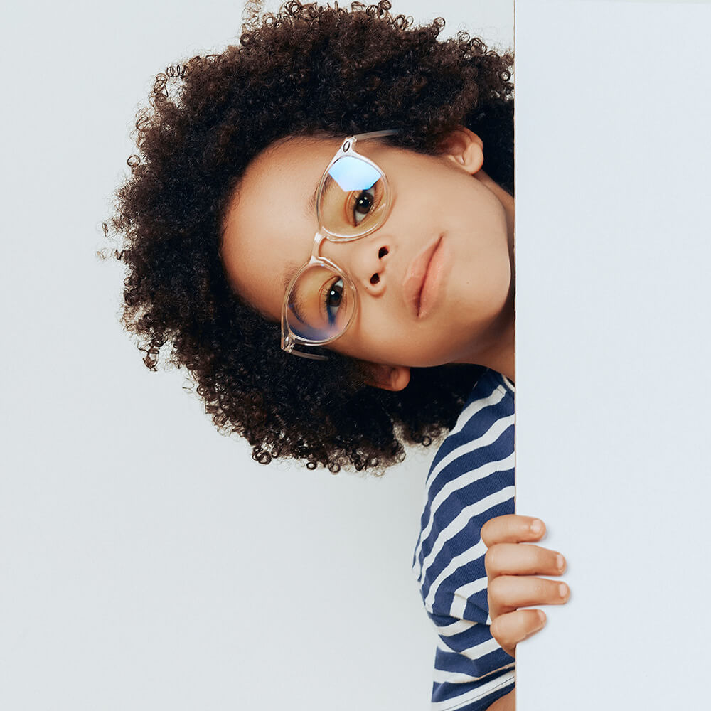 Kidz anti-light blue glasses worn by a child who hides behind a door