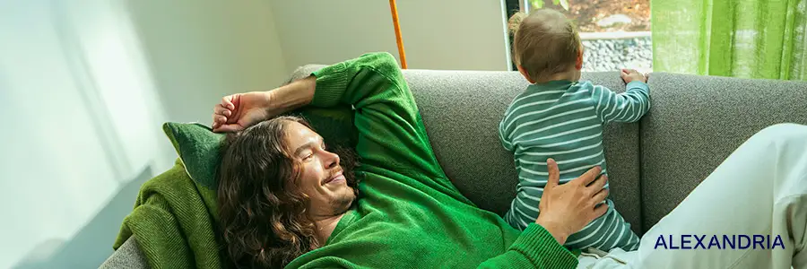 Mannen ligger på soffan och barnet tittar ut genom fönstret.