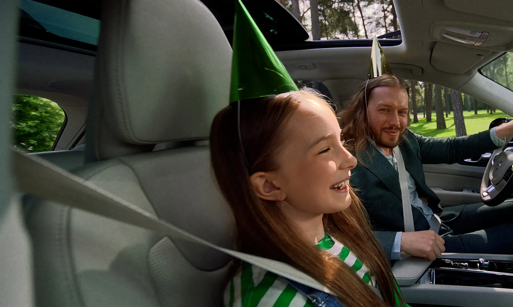 En flicka och en man i bilen med festhattar på huvudet.