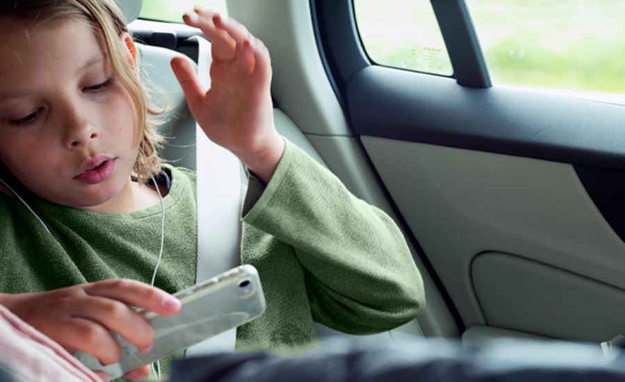 Ett barn sitter i bilen och tittar på sin telefon.