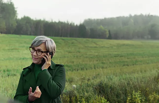 En kvinna pratar i telefon vid kanten av en åker.