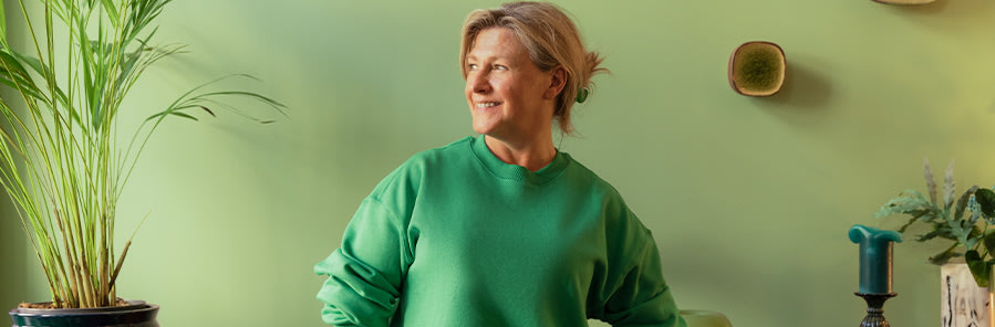 En kvinna i grön tröja tittar ut genom fönstret och ler.